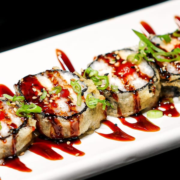 Four Himiko Sushi rolls, deep-fried, drizzled with sauce, sesame seeds, and green onions.