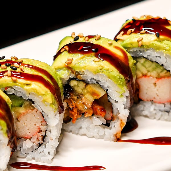 Himiko Sushi's avocado-topped sushi rolls with dark sauce and sesame seeds on a white plate.