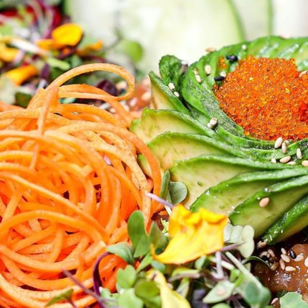 Close-up of a sushi dish with spiralized carrots, sliced avocado, and orange tobiko.