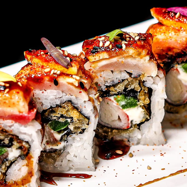 Close-up of Himiko Sushi's specialty sushi rolls, topped with glazed eel, sesame seeds, and microgreens.