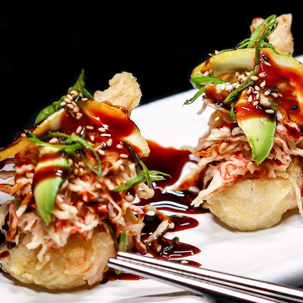 Two Himiko Sushi tempura bites with crab, avocado, sesame seeds, and sauce on a white plate.